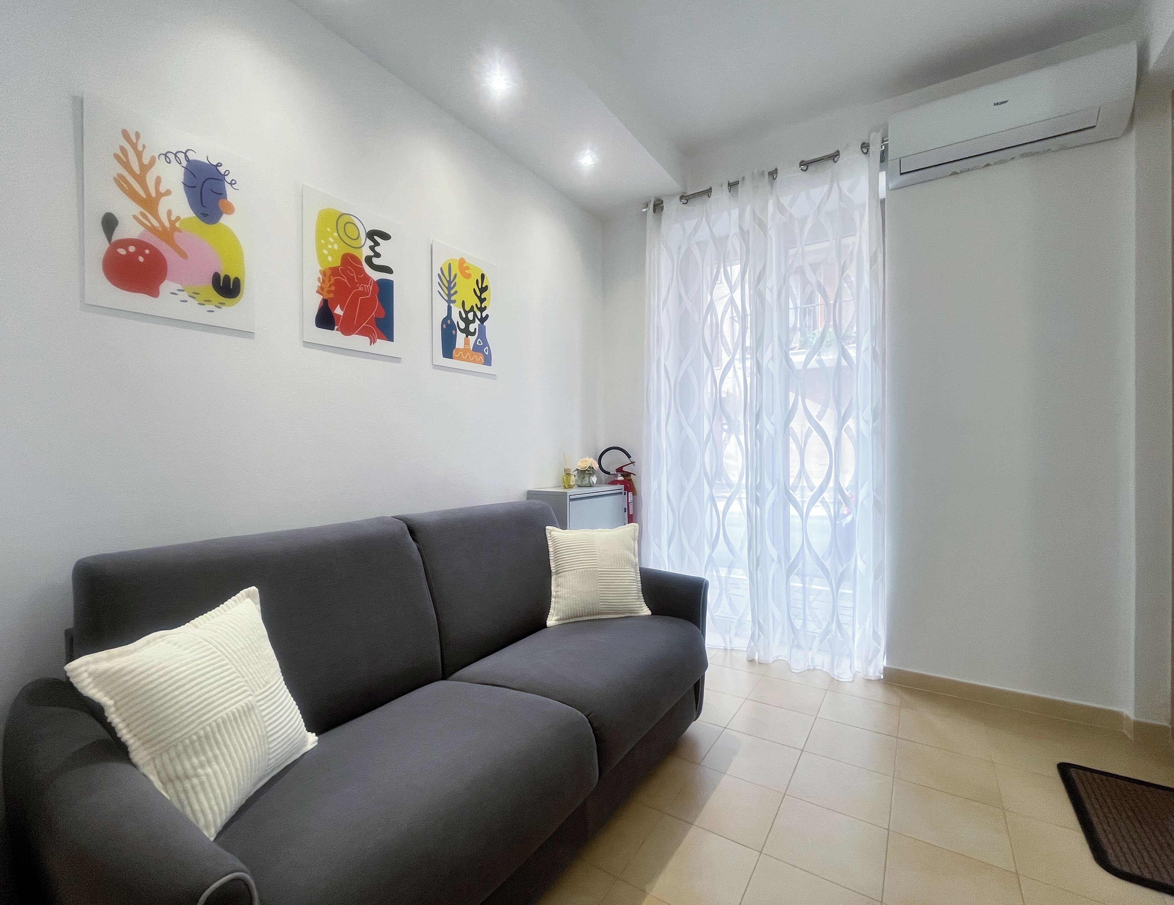 Un salon moderne avec un canapé gris, des coussins blancs et des œuvres d’art abstraites et colorées accrochées au mur.