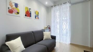 Un salon moderne avec un canapé gris, des coussins blancs et des œuvres d’art abstraites et colorées accrochées au mur.