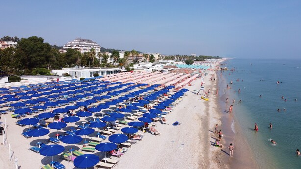 A beach with rows of blue umbrellas and sun loungers.
