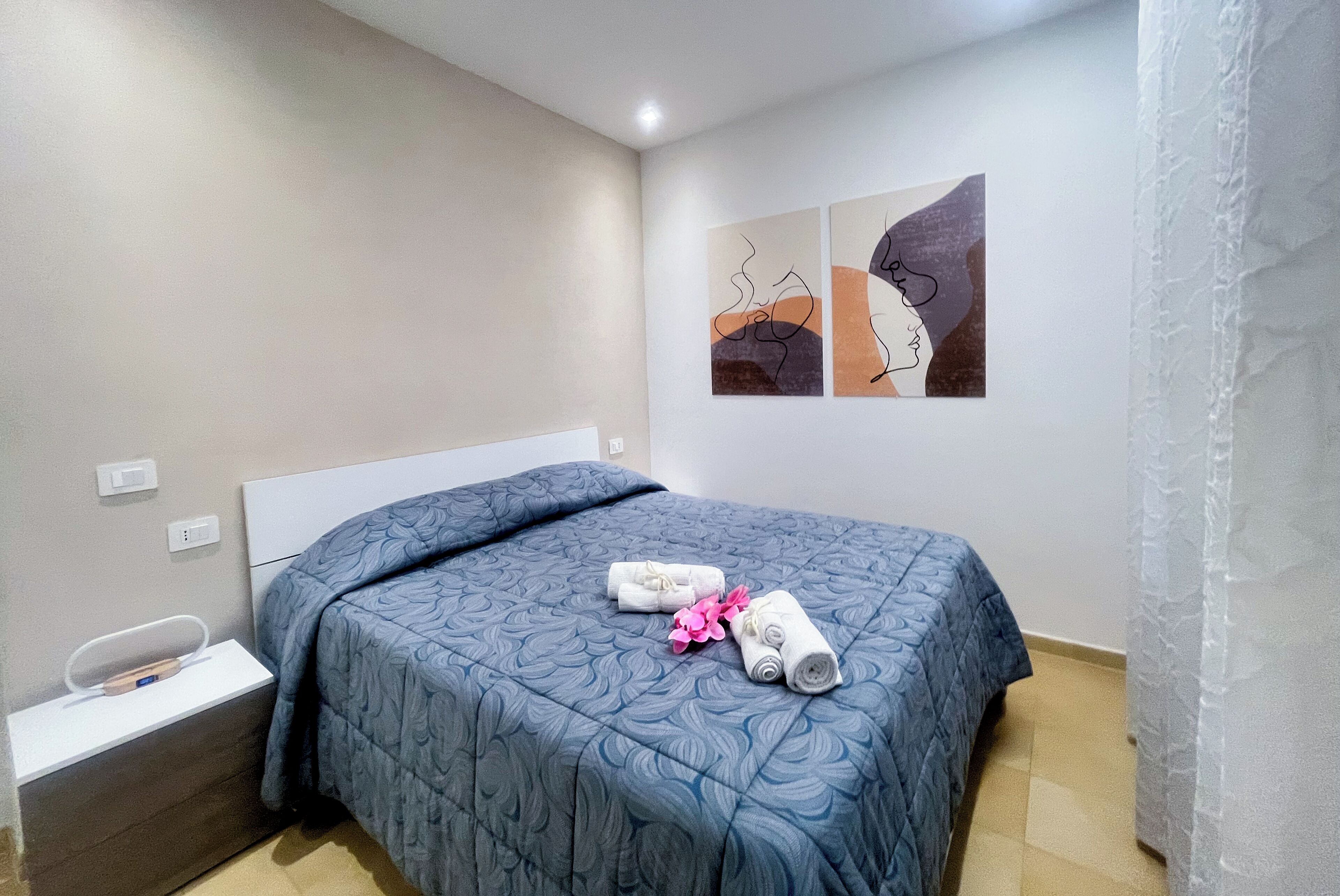Un dormitorio con cama, mesita de noche y dos obras de arte colgadas en la pared.