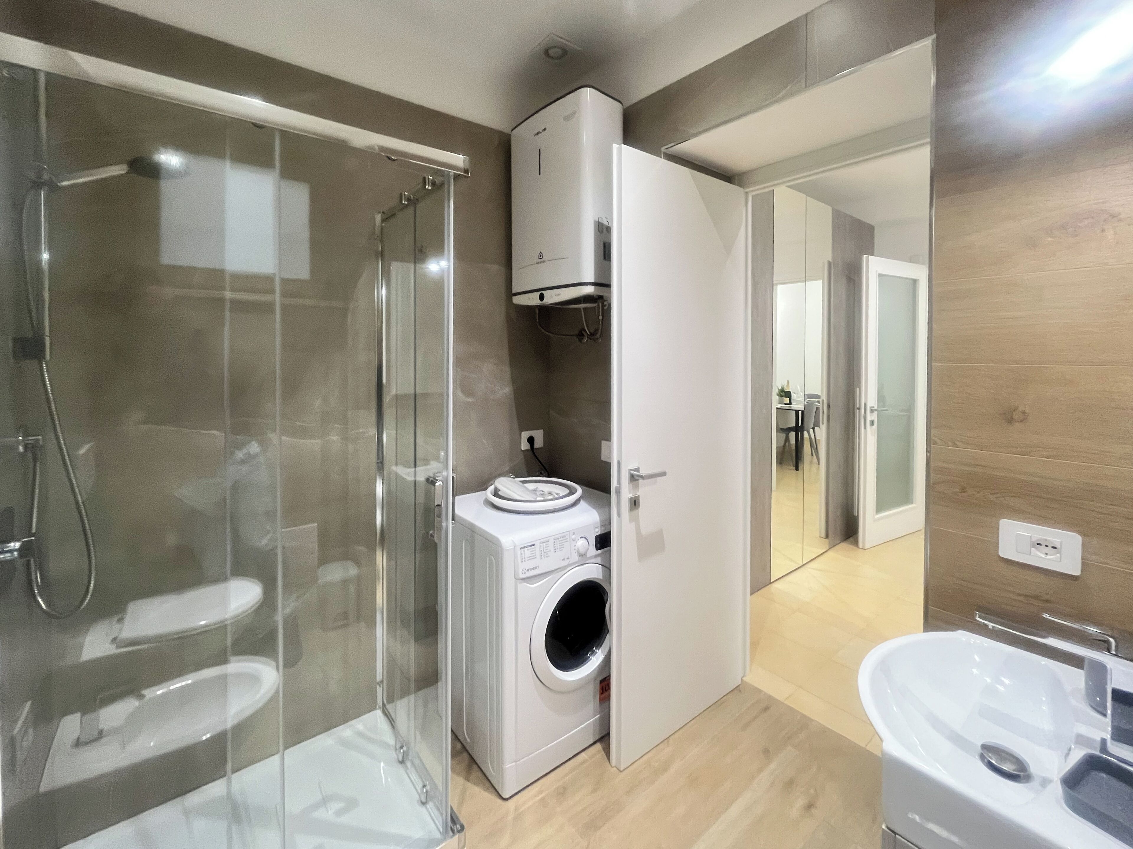 Ein modernes Badezimmer mit einer gläsernen Duschkabine, einer integrierten Waschmaschine und einem Waschbecken.