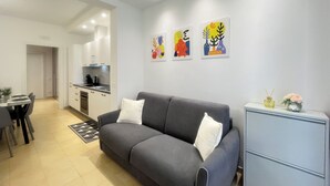 A modern living room with a grey sofa, a small cabinet, and a dining area with a table and chairs.