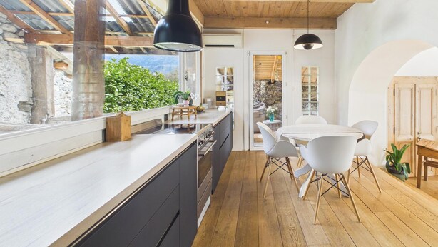 A modern kitchen with a wooden ceiling, a large window, and a dining area with white chairs. - Charming country house near Lake Leman (Lully)
