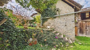 A rustic stone building with a wooden staircase, a dog, and a garden with various plants and flowers. - Charming country house near Lake Leman (Lully)