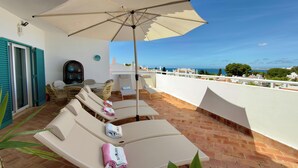 Eine Dachterrasse mit Liegestühlen, einem Tisch und einem Sonnenschirm.