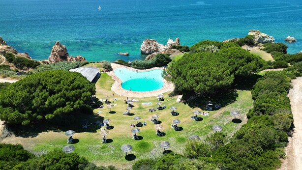 Luftaufnahme eines Resorts mit Schwimmbad, Strandstühlen und üppiger Vegetation.