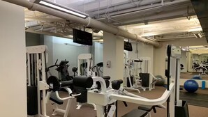 Een sportschool met diverse fitnessapparaten, een aan de muur bevestigde televisie en trainingsballen op een tafel.