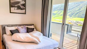 Une chambre à coucher avec un lit, des oreillers, un tableau encadré et un balcon donnant sur un paysage verdoyant.