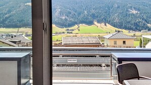 Une vue depuis un balcon donnant sur un paysage montagneux, avec une voie ferrée et des bâtiments au premier plan.