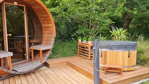 A wooden hot tub with a bench inside, surrounded by a deck and potted plants.
