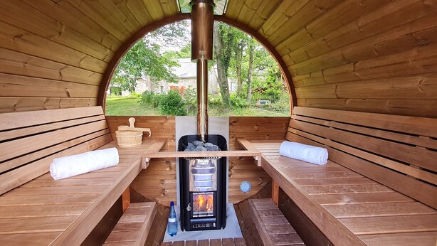 A wooden sauna with benches and a central wood-burning stove.