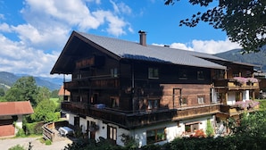 Un chalet en bois à plusieurs étages, doté de balcons et entouré de verdure et de montagnes.