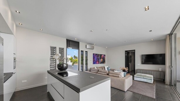 Una cocina moderna con una isla central, una zona de comedor con sofá y un televisor grande.