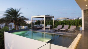 Una piscina infinita en la azotea con sillones de descanso y un área de estar techada.