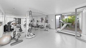 Un gimnasio moderno con diversos equipos de ejercicio, un espejo grande y vistas a zonas verdes a través de un ventanal.