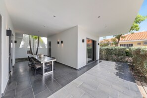 A modern patio with a dining table and chairs, surrounded by a stone wall and a view of a residential area.