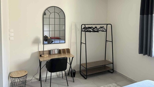 A compact room with a desk, a chair, a hanging clothes rack, a small round table, and a large window with a grid design. - Le Jardin d'Elusa - Gîte Le Chai (**** 4 stars) (Eauze)