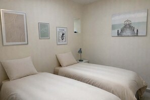 Un dormitorio con dos camas, una mesita de noche con lámpara y tres obras de arte enmarcadas en la pared.