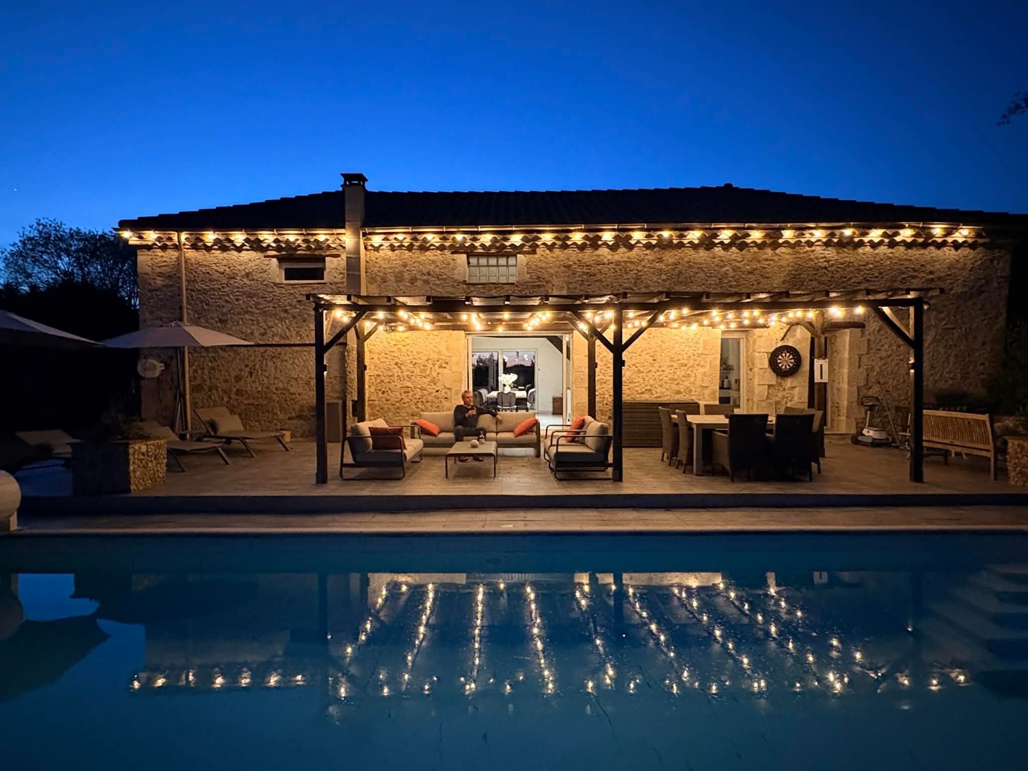 Eine Poolterrasse mit Sitzmöglichkeiten im Freien und Lichterketten.