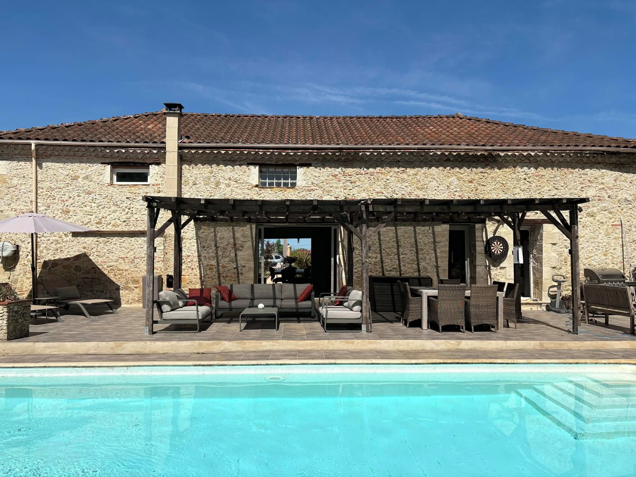 A stone building with a pool, outdoor seating, and a pergola.