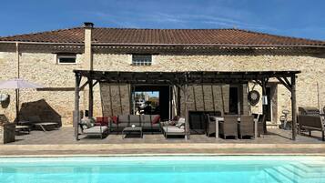 A stone building with a pool, outdoor seating, and a pergola.