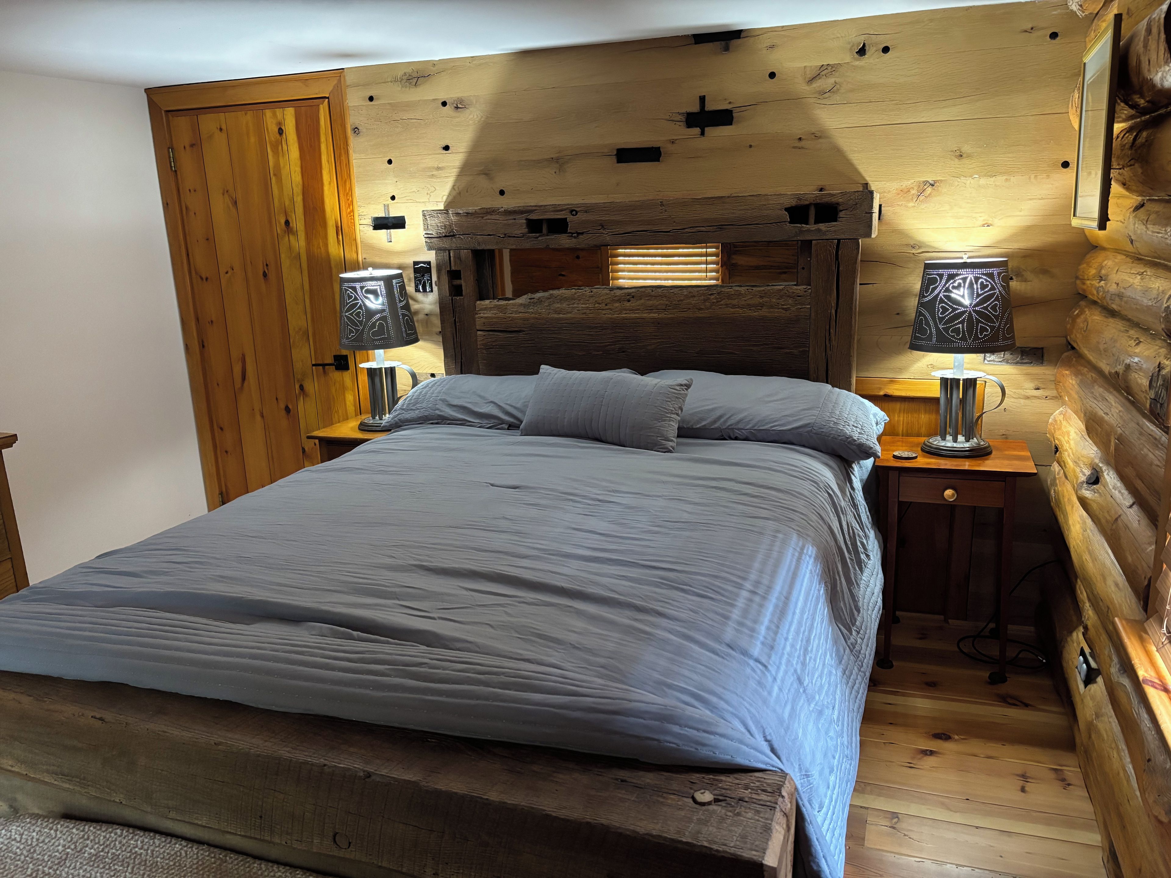 A wooden cabin-style bedroom with a bed, two bedside lamps, and a wooden headboard.