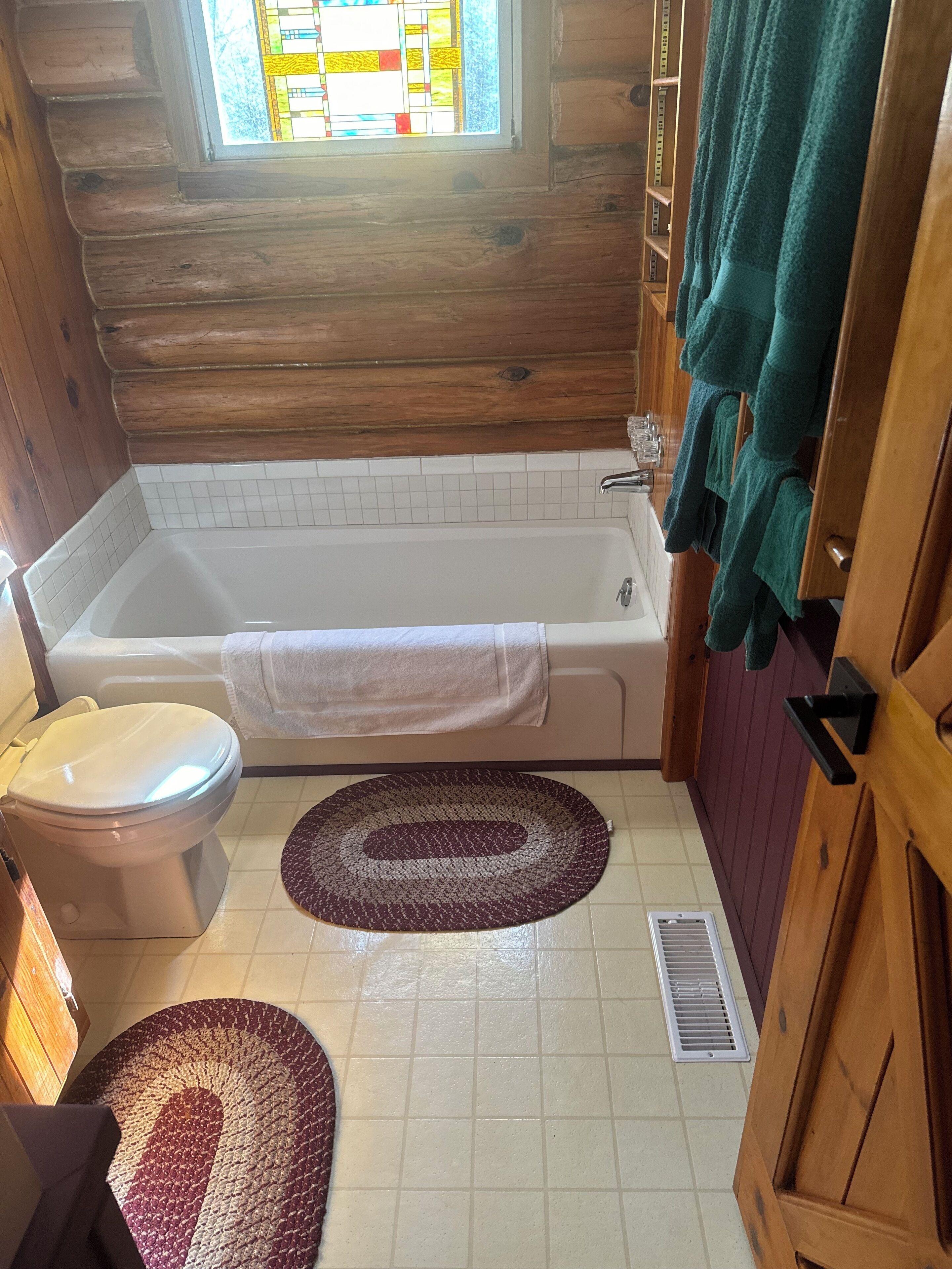 A wooden cabin bathroom with a bathtub, toilet, and two rugs.