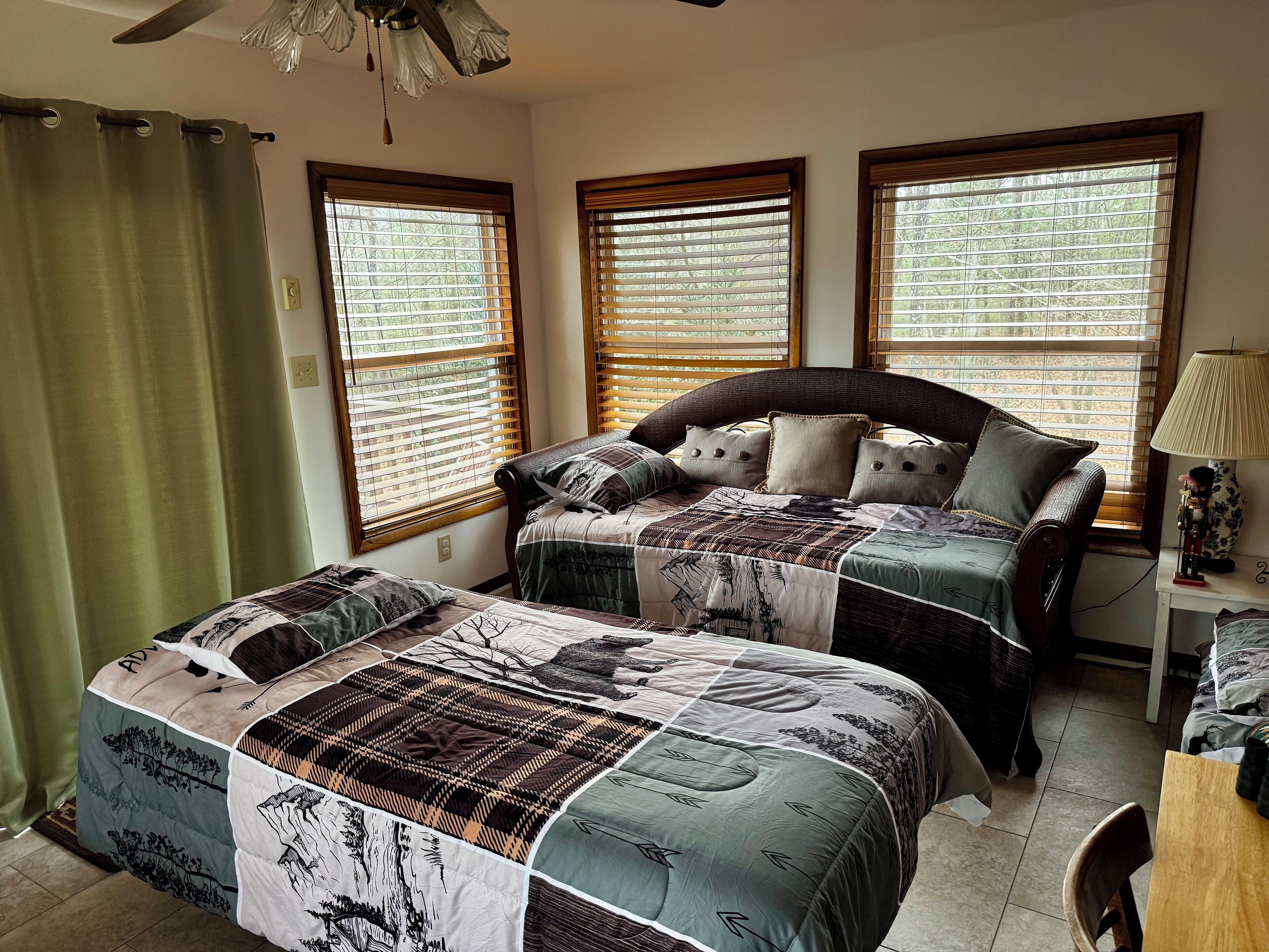 A bedroom with two beds, a ceiling fan, and three windows with blinds.