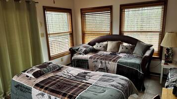 A bedroom with two beds, a ceiling fan, and three windows with blinds.