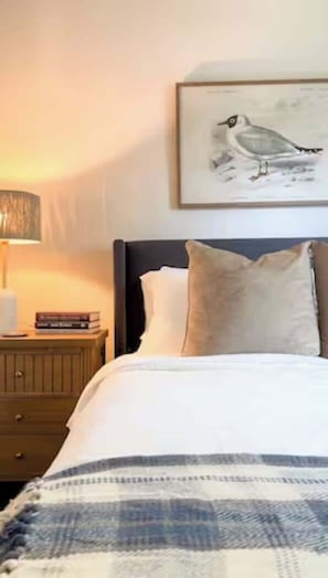 A neatly made bed with a striped blanket, a pillow, and a framed bird painting on the wall above. - Pet-Friendly Home with Fenced Yard (Raleigh)