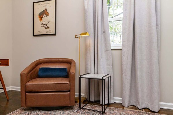 A brown leather armchair with a blue cushion, a small side table, a floor lamp, and a framed horse illustration on the wall.