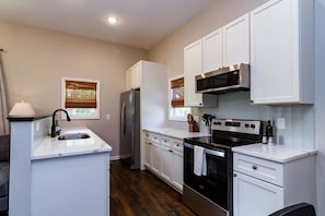 A modern kitchen with white cabinets, stainless steel appliances, a built-in oven, and a window with blinds. - Pet-Friendly Home with Fenced Yard (Raleigh)