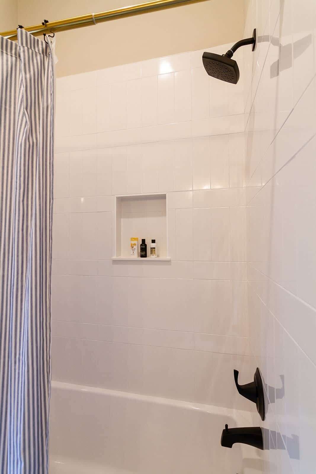 A shower area with a handheld showerhead, a wall-mounted showerhead, and a shelf with toiletries.