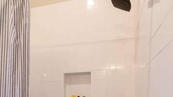 A shower area with a handheld showerhead, a wall-mounted showerhead, and a shelf with toiletries.