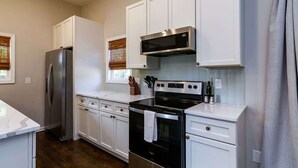 A compact kitchen with white cabinets, a stainless steel refrigerator, a black oven, and a microwave above the stove. - Pet-Friendly Home with Fenced Yard (Raleigh)