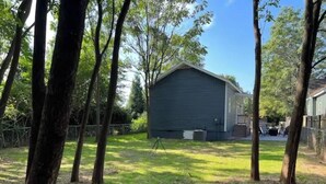 A single-story building with a gabled roof, surrounded by trees and a grassy yard. - Pet-Friendly Home with Fenced Yard (Raleigh)