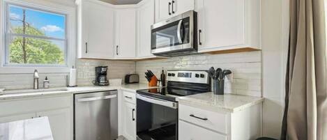 A modern kitchen with white cabinets, a microwave, a stove, and a dishwasher.