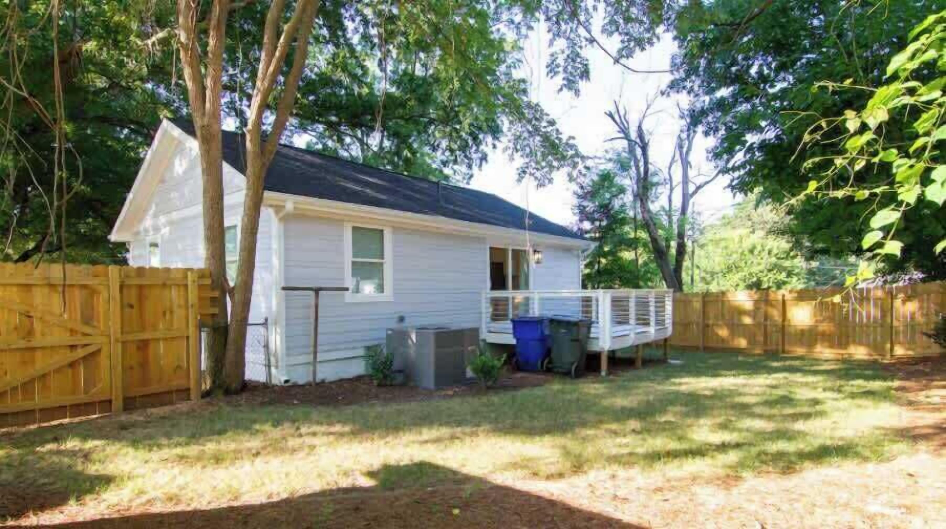 A single-story house with a front porch, a fenced backyard, and a wooden deck.