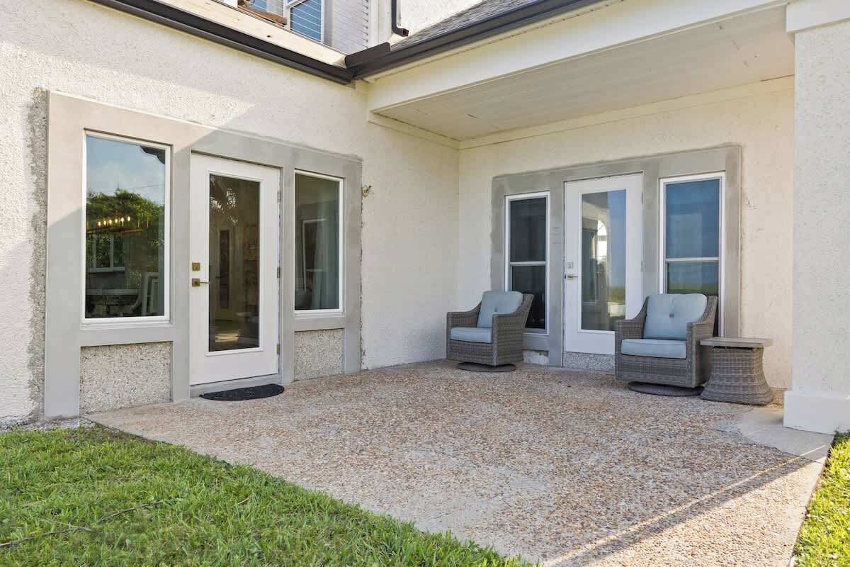 Ein überdachter Patio-Bereich mit zwei Korbstühlen und einem kleinen Tisch, einer Tür und einem Fenster.