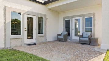 A covered patio area with two wicker chairs and a small table, a door, and a window.