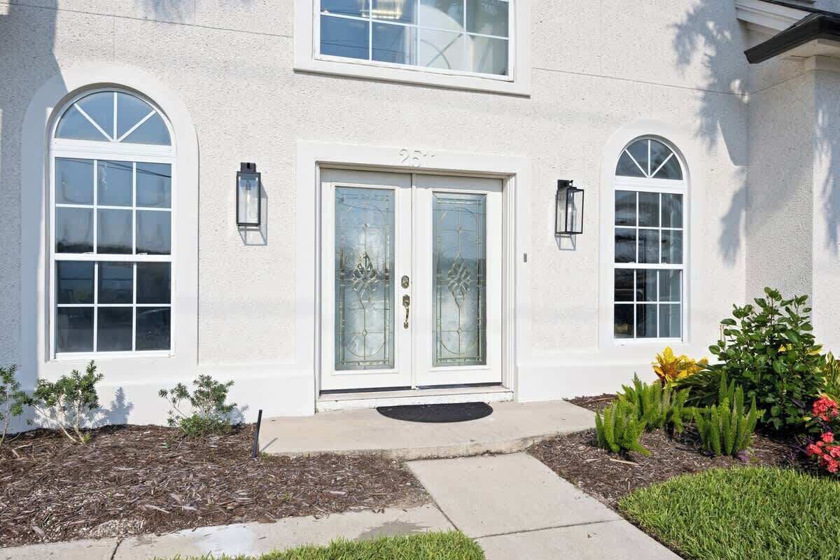 A two-story house with a white exterior, a front door with glass panels, and two arched windows on the upper floor.