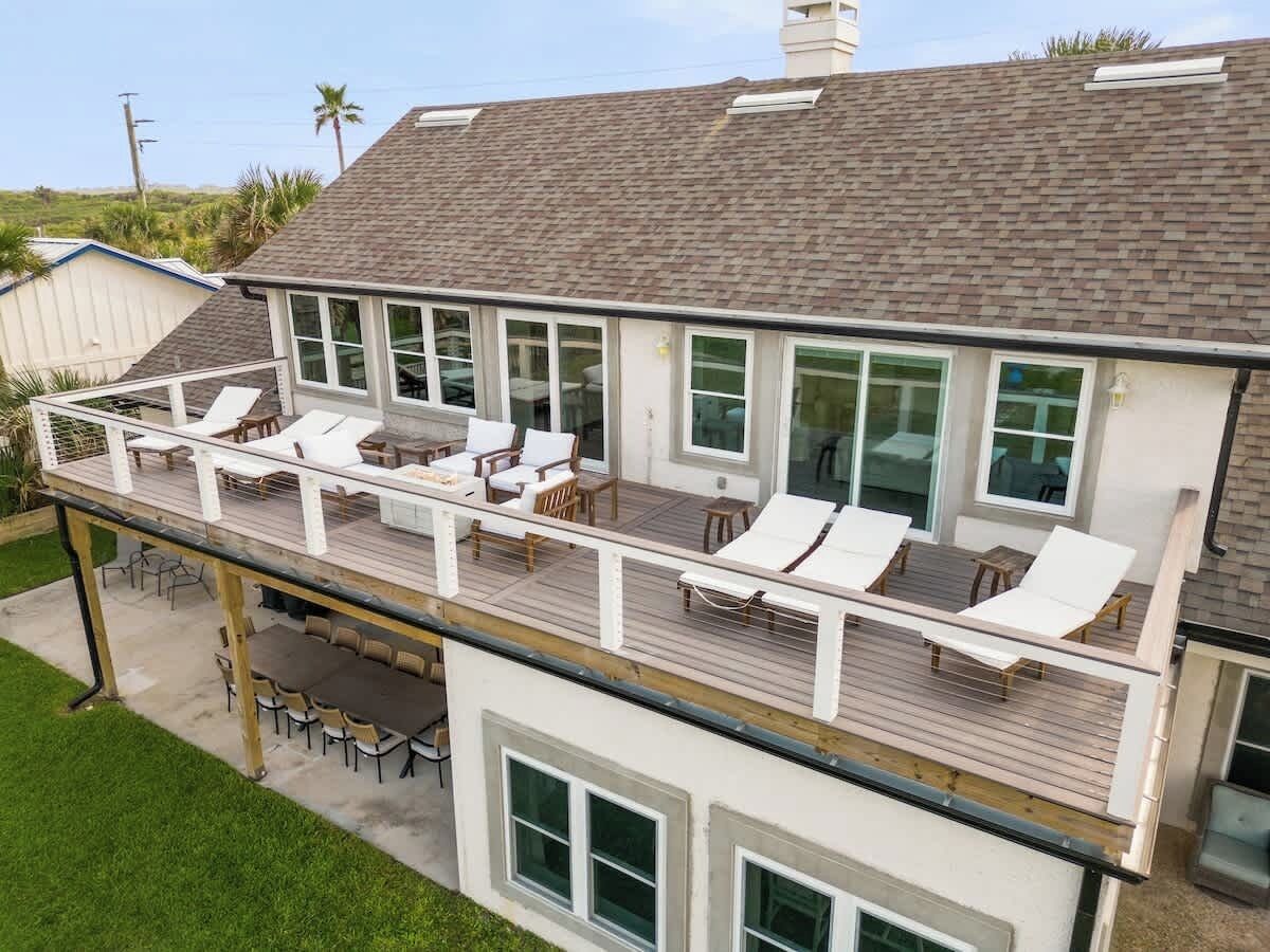 A two-story house with a deck, outdoor seating, and a large window overlooking a grassy area.
