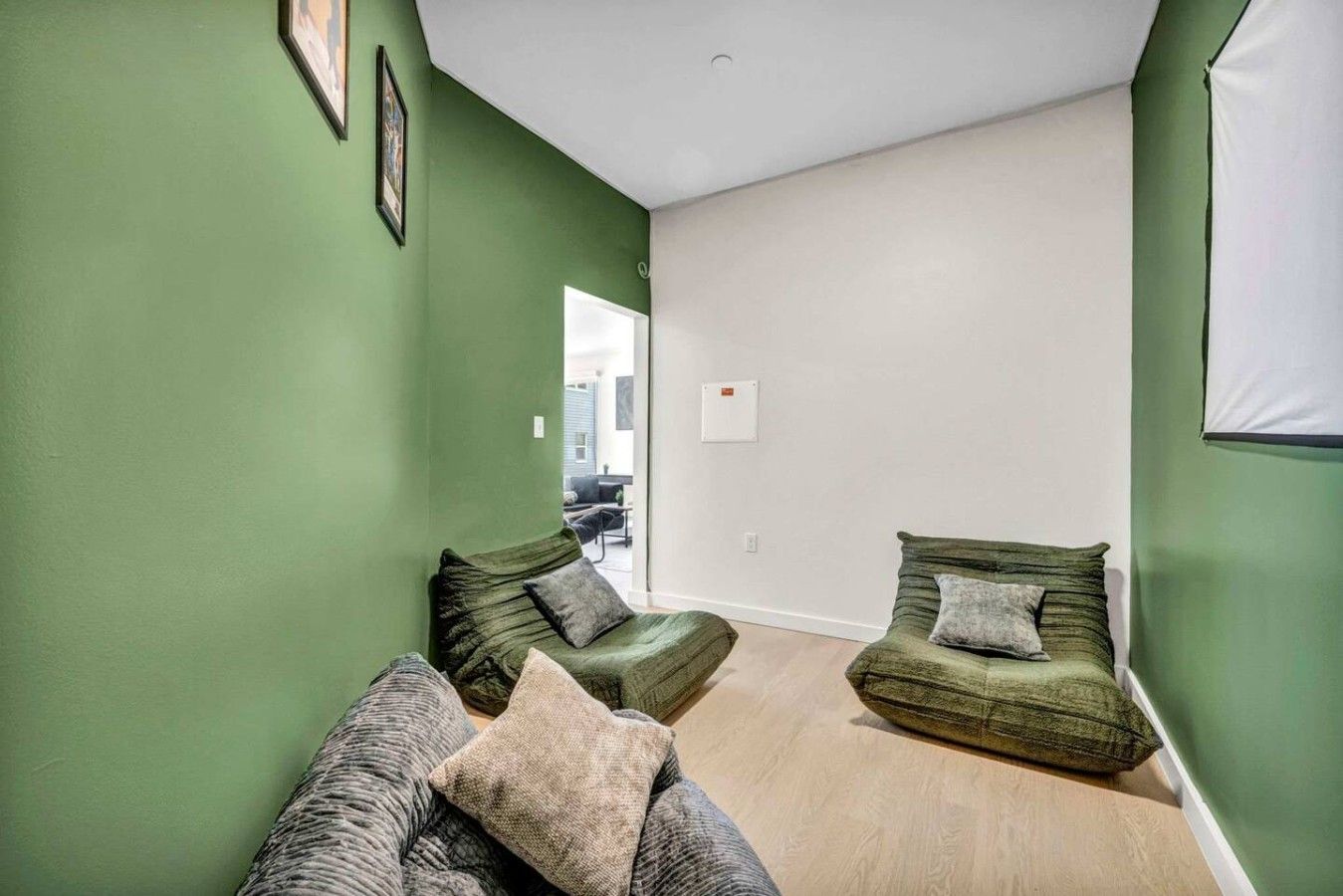 A room with two green upholstered sofas, a wooden floor, and a white wall.