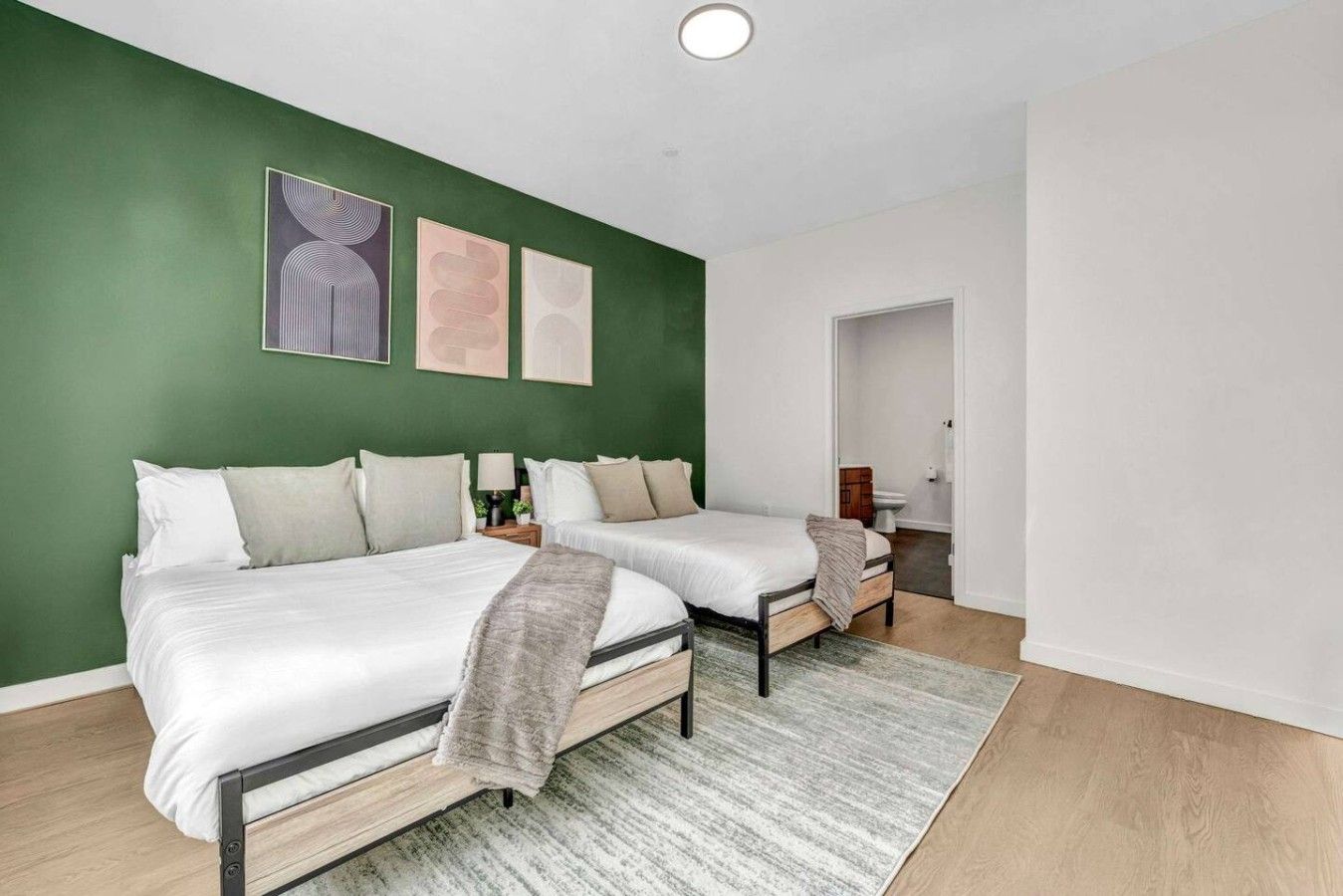 Une chambre d’hôtel avec deux lits, un mur d’accent vert et un tapis gris.
