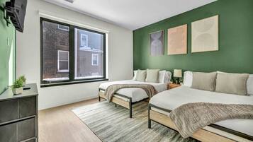 A modern bedroom with two beds, a large window, and green walls.
