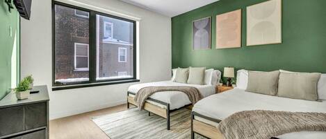 Un dormitorio moderno con dos camas, un ventanal grande y paredes verdes.