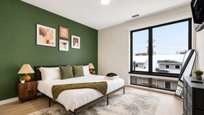 Quarto moderno com cama, mesas de cabeceira, uma janela ampla e obras de arte na parede.