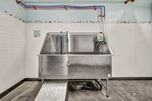 Een rvs-wastafel met een afzuigkap, een zeepdispenser op de muur en een betegelde vloer.