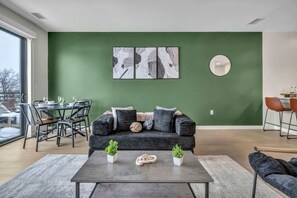 Een moderne woonkamer met een groene accentmuur, een eethoek met een ronde tafel en een bank met kussens.