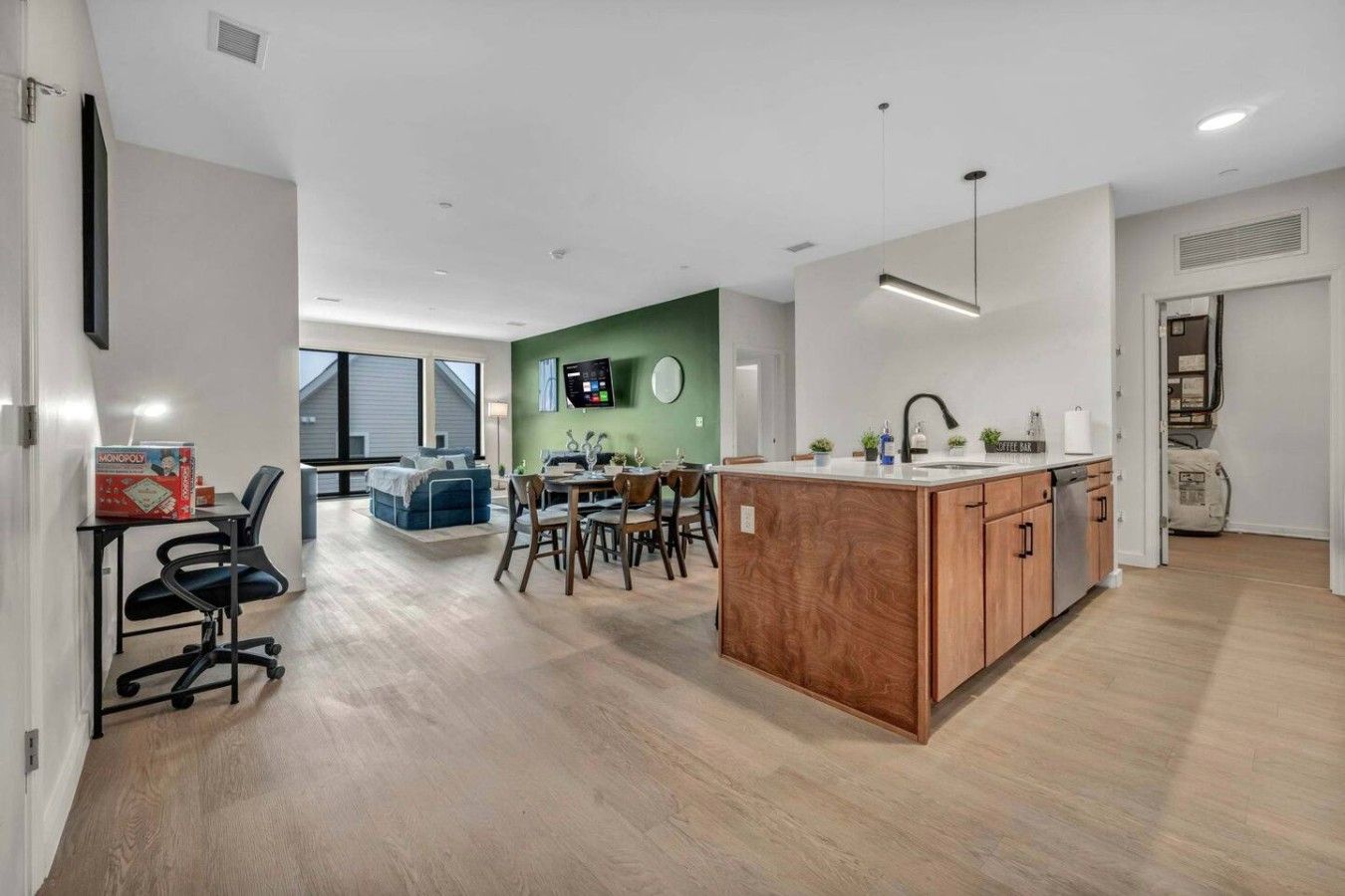 A modern kitchen with a central island, dining area with chairs, and a flat-screen TV mounted on the wall.